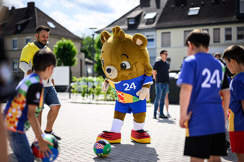 EM-Maskottchen spielt Fußball mit Kindern auf der Straße